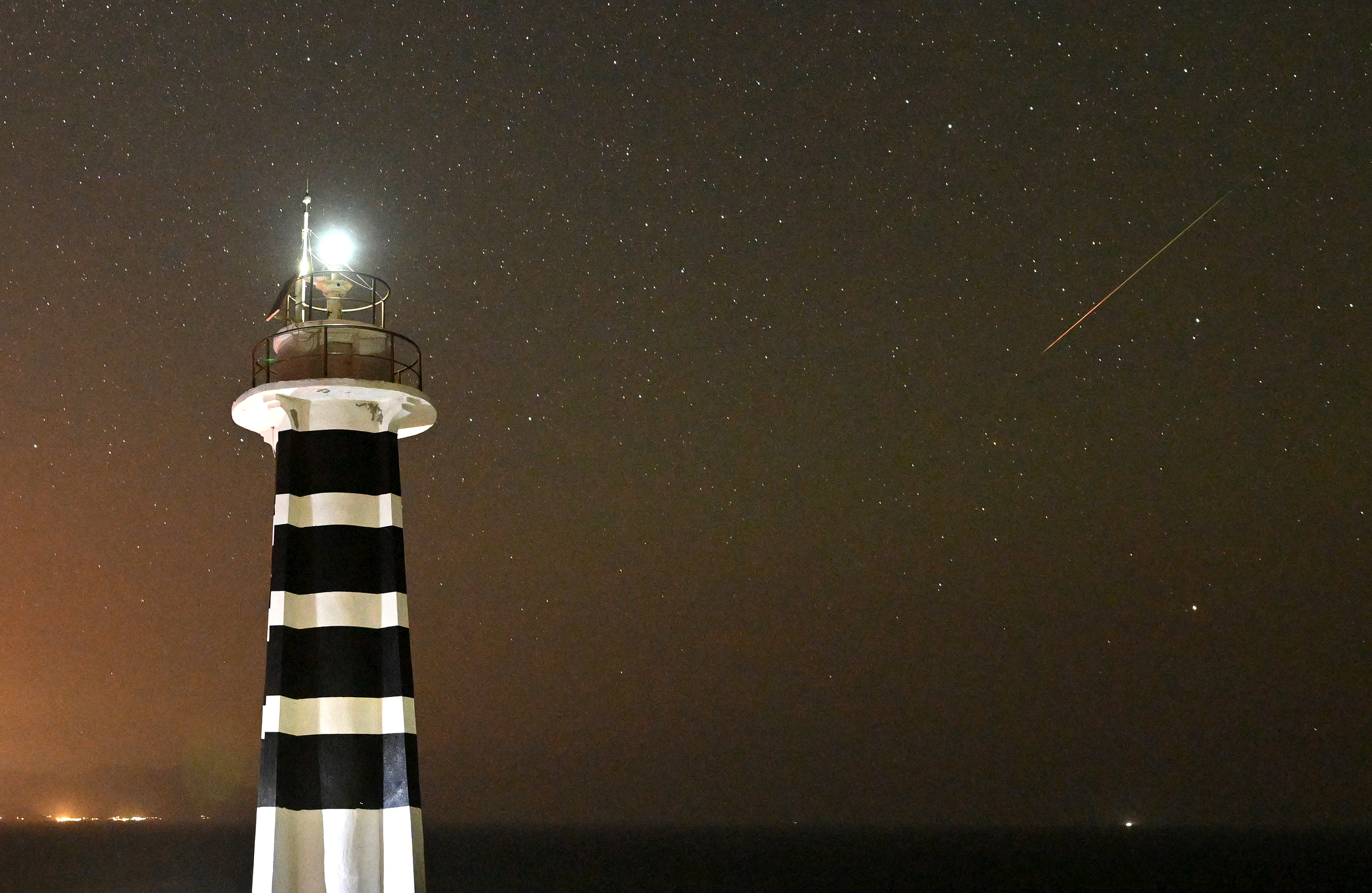 右側にはペルセウス座流星、左側には白と黒の縞模様の明るい灯台が見えます。