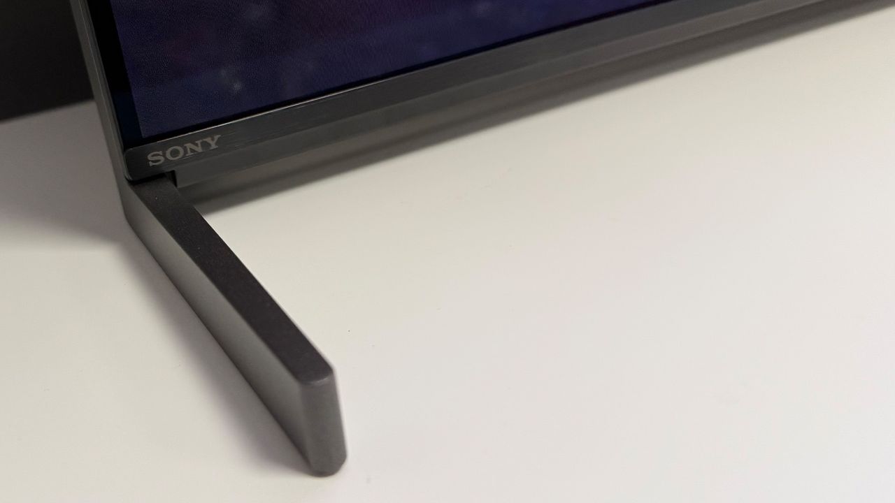 A close-up of one of the blade-style feet at the base of the 55-inch Sony Bravia 8 II QD-OLED TV, seen on a white table.