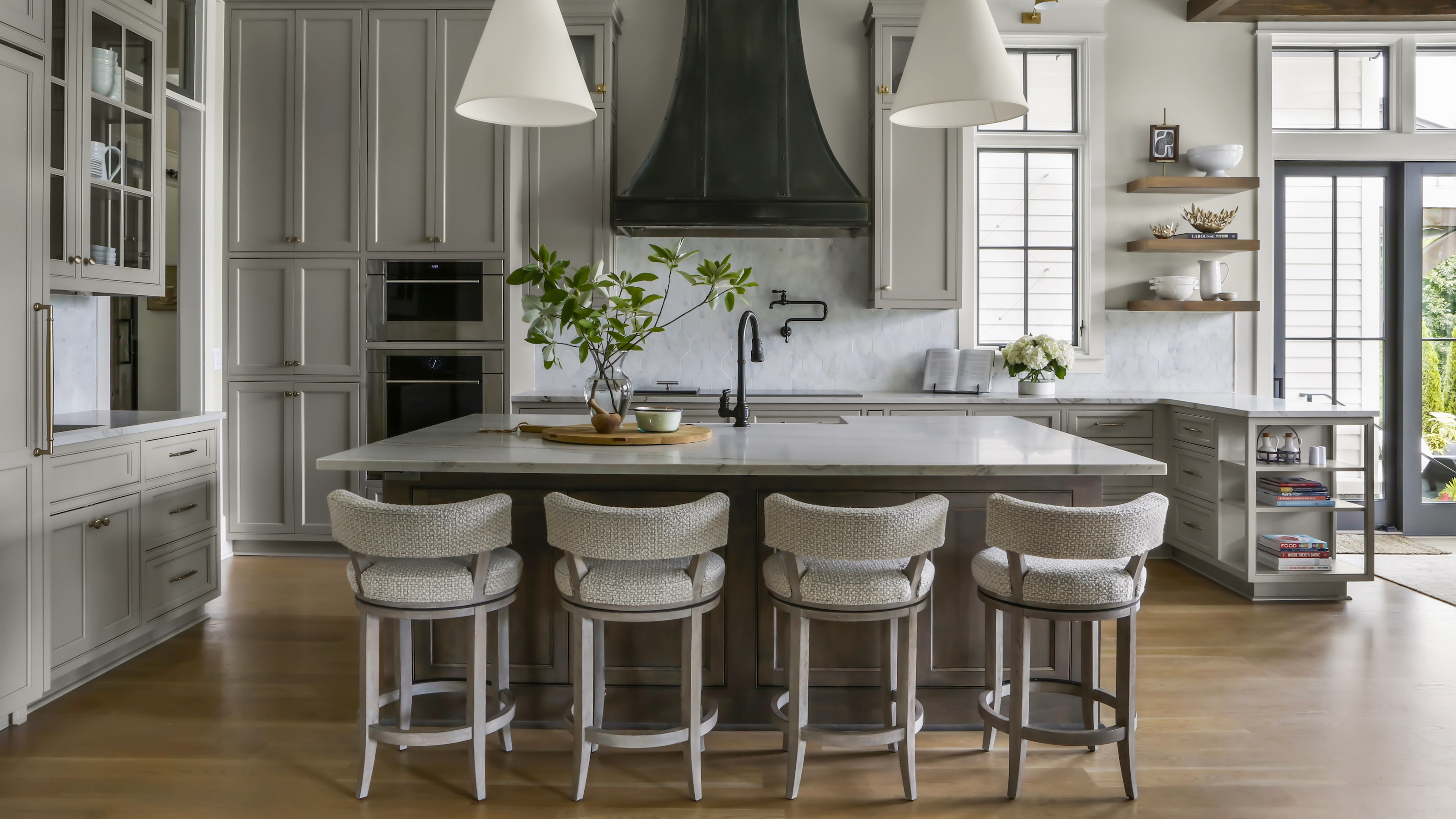 Kitchen with gray cabinets and island with four barstools and pendant lights over