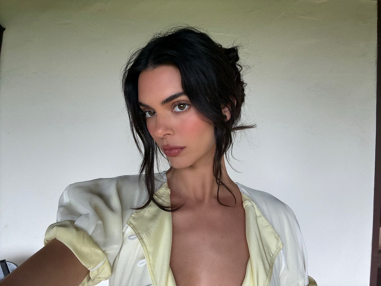 Kendall Jenner taking a selfie wearing a white and yellow top with natural makeup
