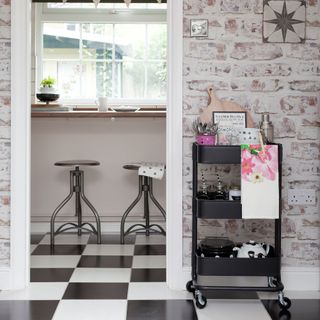 Exposed whitewashed brickwork of kitchen with large black and white checked floor tiles looking through doorway to breakfast bar and stools