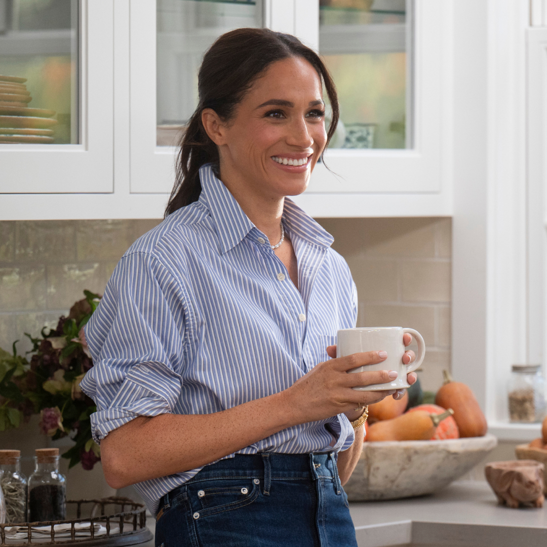 Meghan Markle wearing a blue striped shirt holding coffee cup