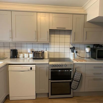 Newly renovated grey kitchen with white backsplash tiles containing many kitchen appliances