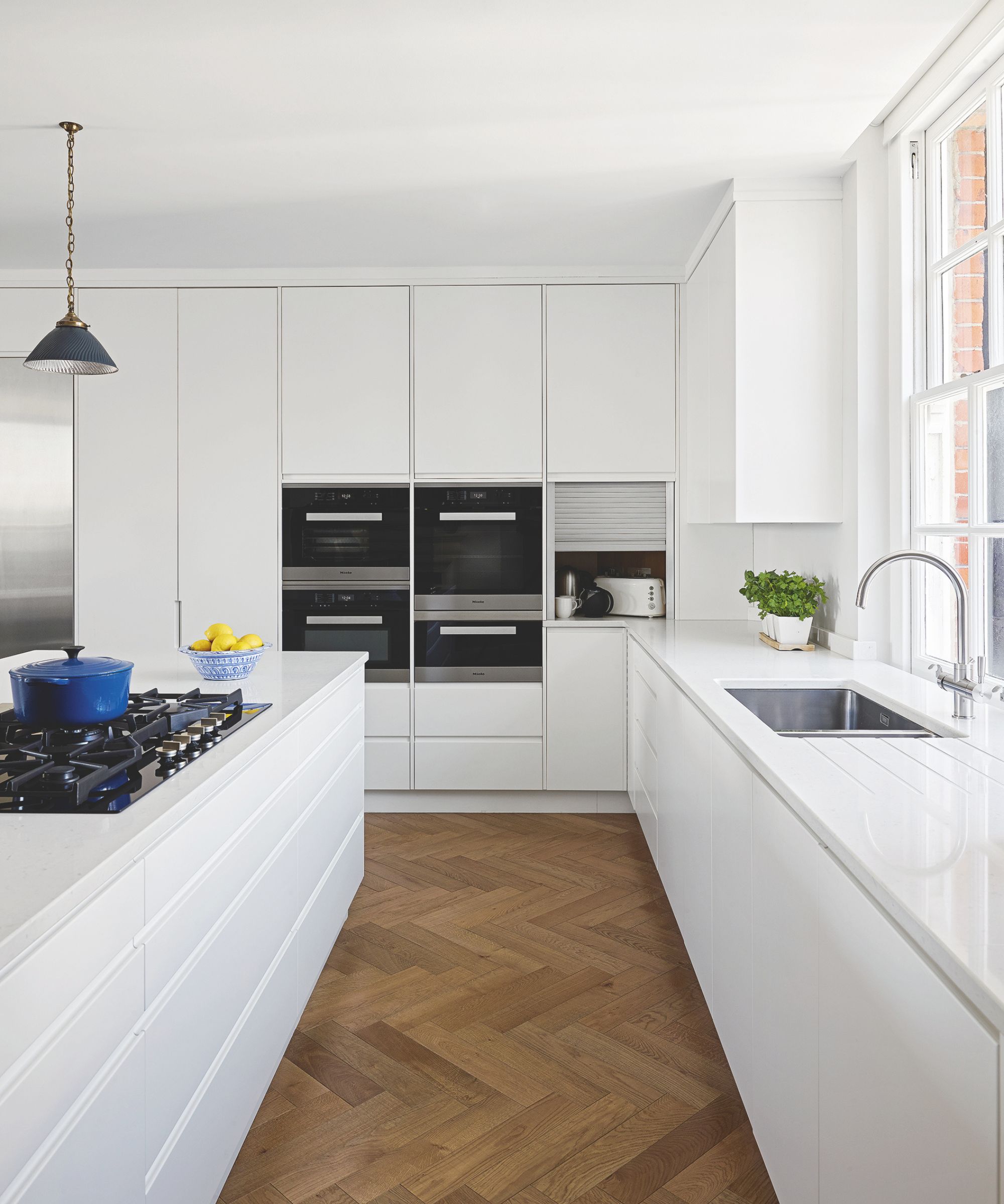 Minimalist kitchen with white built-in cabinets, white island and stove and wood parquet flooring