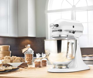 KitchenAid Classic Series Stand Mixer in white on a wooden countertop with biscuits to the side and a big window in the background
