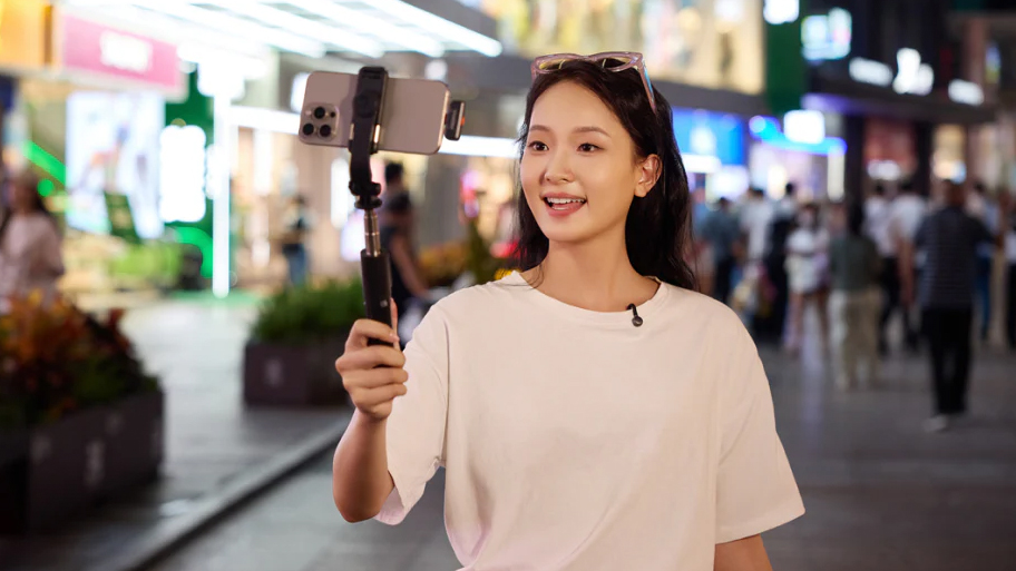 Hollyland Lark M2S used in mobile phone on a selfie stick being held by an individual on a bust street