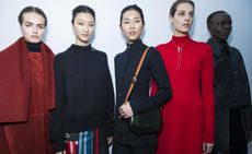 Five female models, one wearing a red coat with cape, one in a black wool sweater, one in a black coat with bag, and one in a red dress