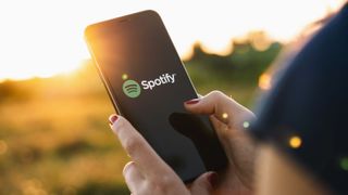 Woman standing in field holding phone in hands with Spotify app onscreen
