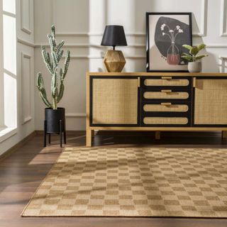 A Kuval Checkered Brown Rug on a wooden floor in front of a dresser with canework