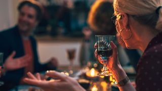 Woman sitting at dinner table talking with alcohol-free drink in one hand, lit by candlelight