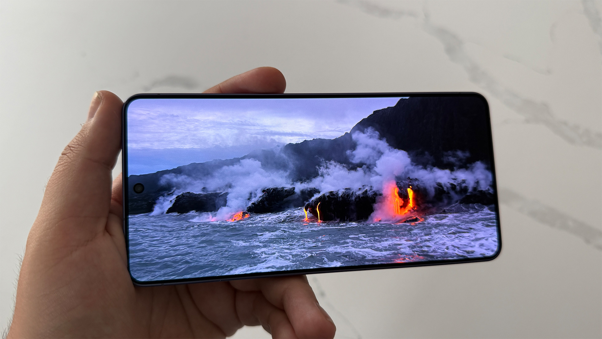 Samsung Galaxy S26 Ultra smartphone held in hand showing fires and coastal scene