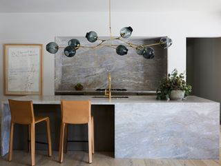 neutral kitchen with stone island and splashback, gray glass pendant and leather barstools
