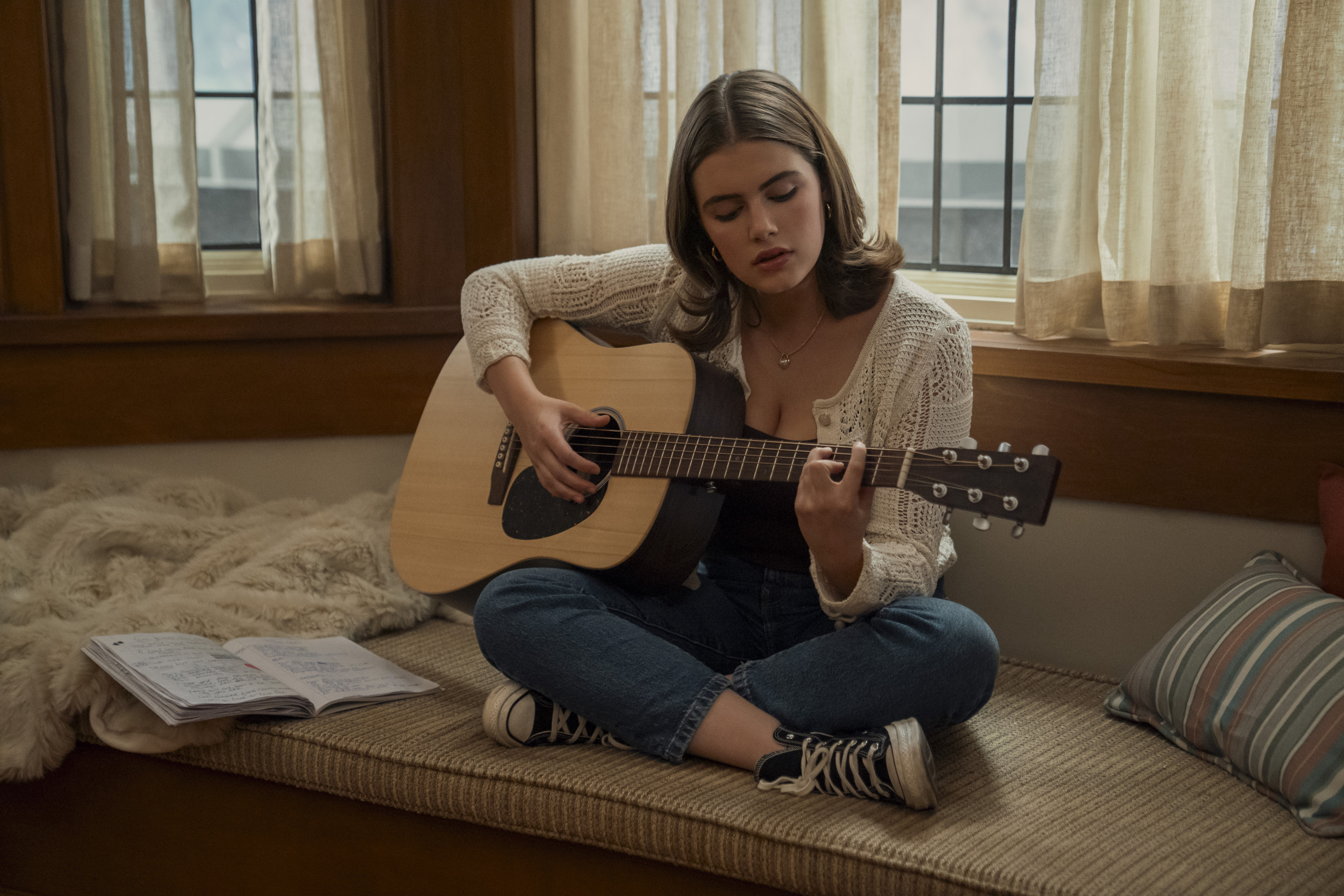 Hannah (Ella Bright) plays an acoustic guitar while sitting by a bay window in season 1 of off campus
