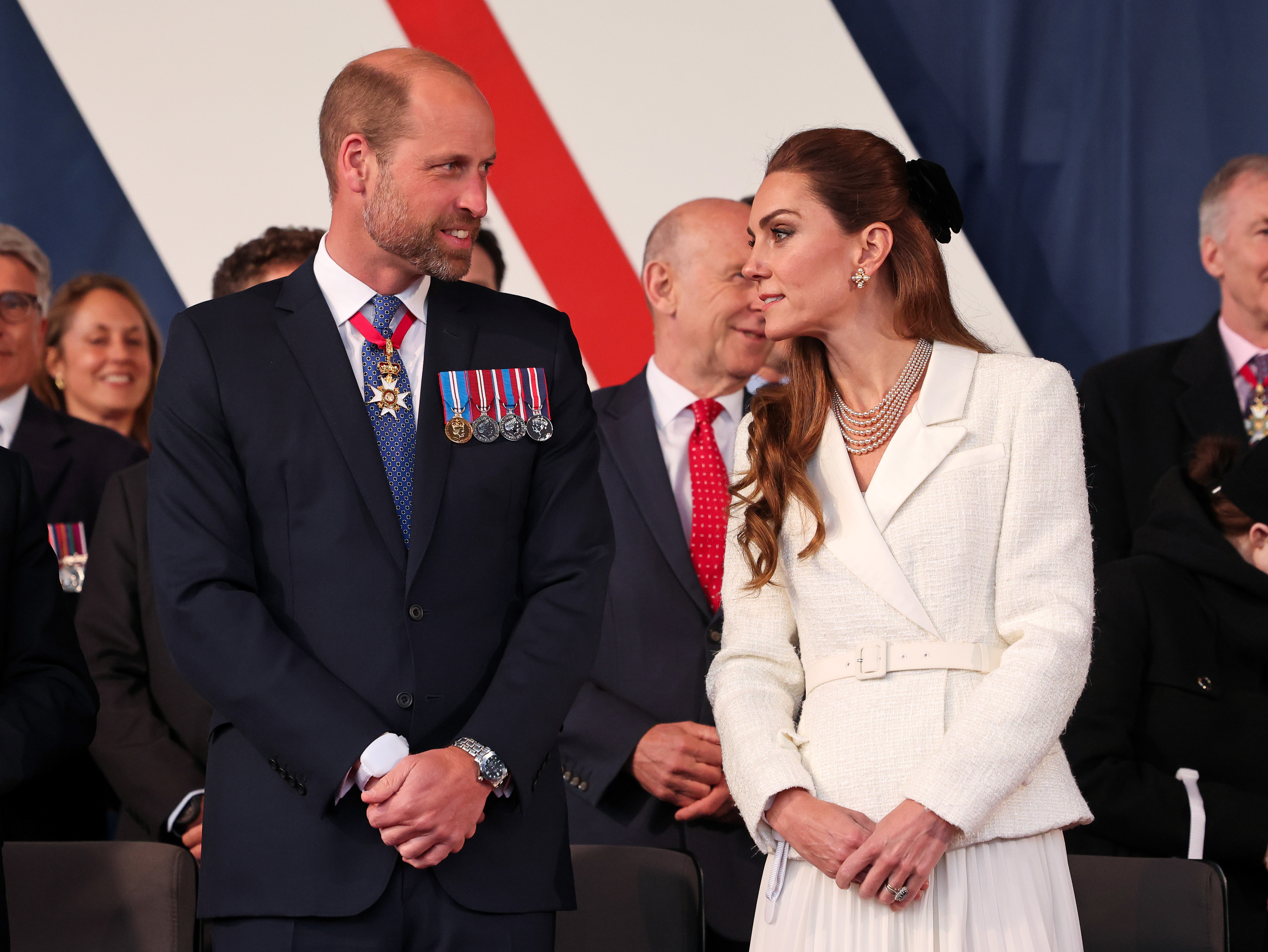 Kate Middleton wearing a white tweed blazer dress talking to Prince William at a VE Day anniversary concert