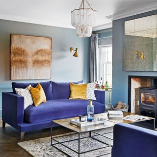 Light blue painted living toom with purple sofas, decorative cushions, coffee table, fireplace