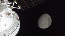 A gray sphere in the darkness of space is seen from a white spacecraft with solar panels to the left of the image. 