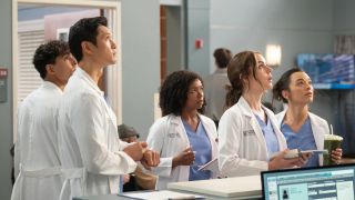 Some of the cast, wearing scrubs and white coats, look up with concern in "Grey's Anatomy" season 20
