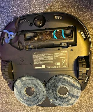 eufy X10 Omni Pro robot vacuum upside down where its two round mop heads and are visible, along with hair in the brushhead