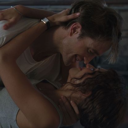 A man in a white T-shirt (actor Robert Pattinson) holds a woman wearing a gray tank top and watch (actor Zendaya) as he dips her in a dance, in the A24 movie 'The Drama.'
