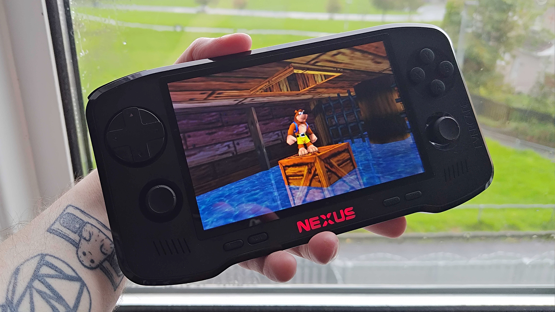 Hand holding Evercade Nexus next to window with Banjo-Kazooie gameplay on screen.
