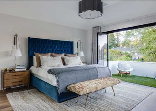 bedroom with blue upholstered bed and bifold doors leading to a balcony with artificial grass