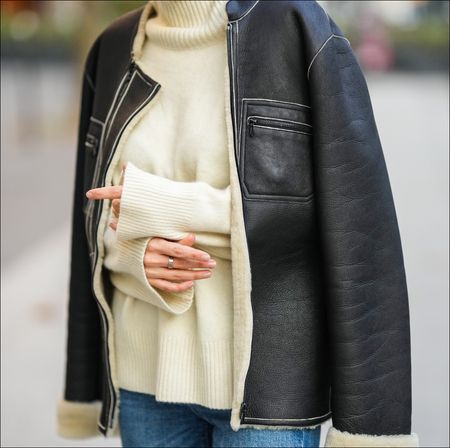 Diane Batoukina @diaanebt wears a white latte cashmere turtleneck pullover from Zara, a black shiny leather with white sheep interior aviator coat from Chanel, blue faded denim large mom jeans pants, during a street style fashion photo session, on November 10, 2021 in Paris, France.