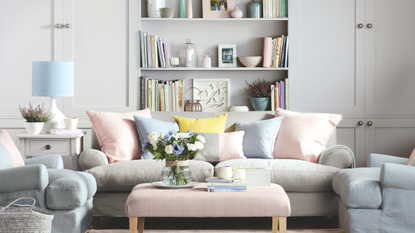 A pastel living room. There is a pink and grey sofa with two blue armchairs and a pink cofee table