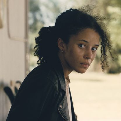 chase infiniti as willa looking to her right wearing a black leather jacket in one battle after another