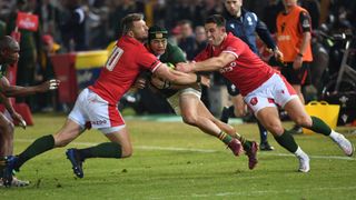 Two Wales rugby players sandwich a South Africa player in a tackle