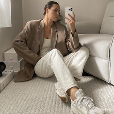 Woman sitting on floor wears beige blazer, white jeans and white trainers
