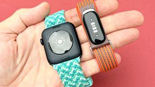 Close-up of the Apple Watch SE 3 and Fitbit Air in a user's hand against a bright, colorful background