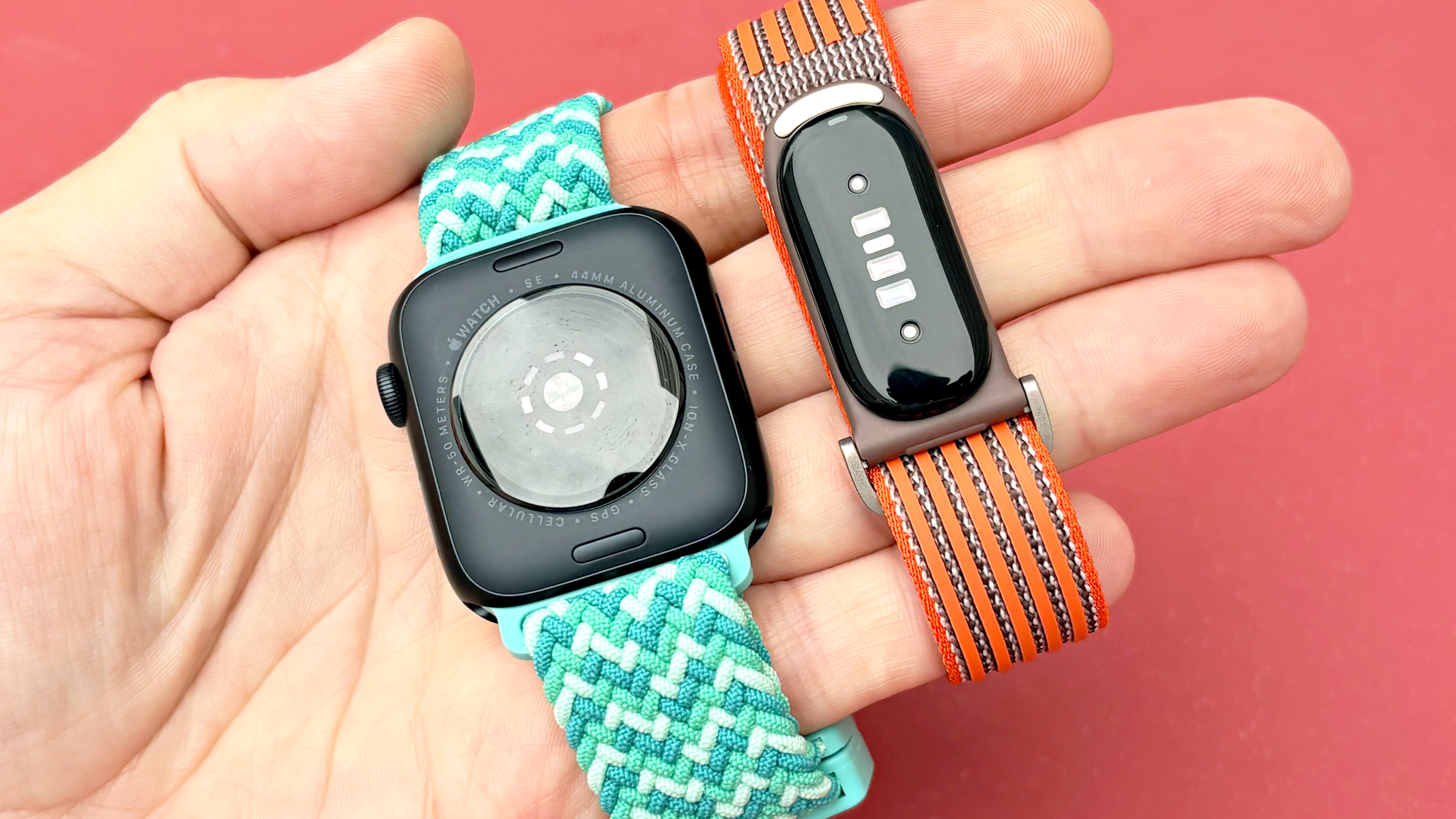 Close-up of the Apple Watch SE 3 and Fitbit Air in a user's hand against a bright, colorful background