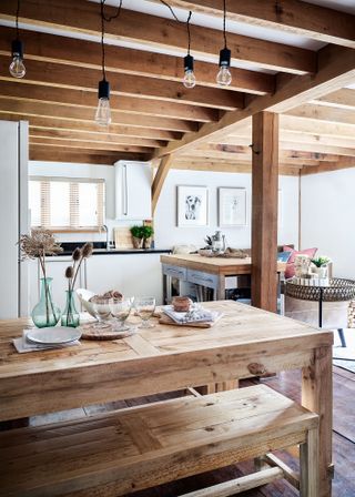 compact kitchen dining space with beams and bare light bulb pendant lights and bench seating under wooden table