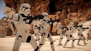 A group of Stormtroopers in white armor advance across a rocky, desert landscape, aiming their blaster rifles.