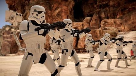 A group of Stormtroopers in white armor advance across a rocky, desert landscape, aiming their blaster rifles.