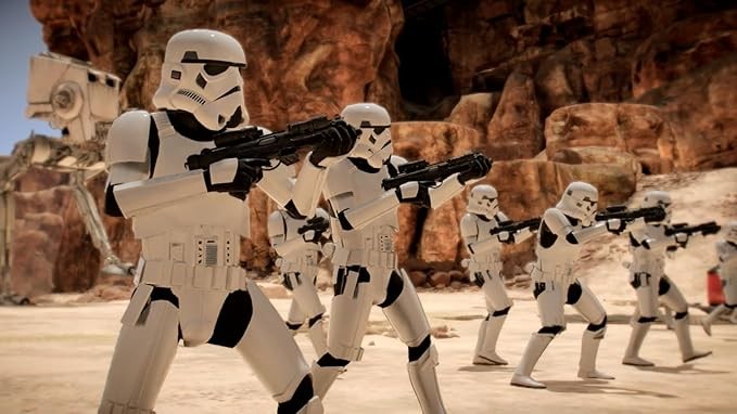 A group of Stormtroopers in white armor advance across a rocky, desert landscape, aiming their blaster rifles.
