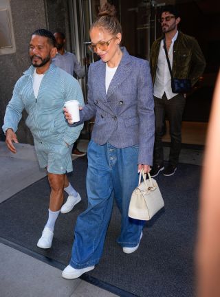 Jennifer Lopez wearing a tailored blue blazer with wide-leg Gucci jeans, white sneakers, and a white Hermès Birkin bag in New York City July 2024