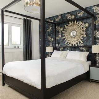 bedroom with cream carpet, an elegant dark green, black and floral wallpaper and a black four poster bed with white covers
