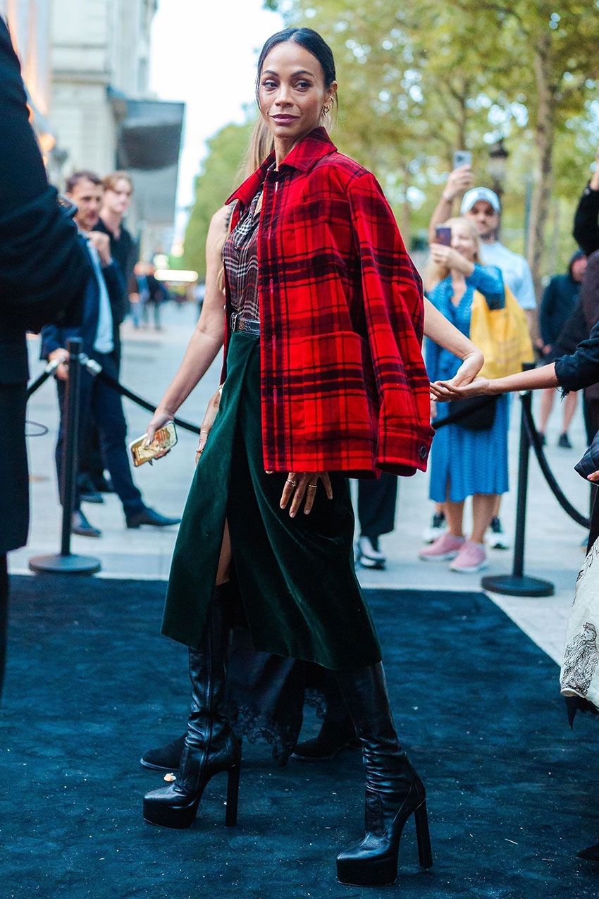 Zoe Saldana wearing a red plaid coat, plaid button down, velvet green skirt, and black leather knee-high boots