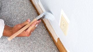 Person painting wall next to skirting board with masking tape on