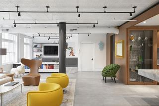 Soho Loft by Ghislaine Viñas and Alexander Butler Architects features curved chairs in yellow and brown, a sheep animal object, a low book side-board, a TV and shelf units on the wall.