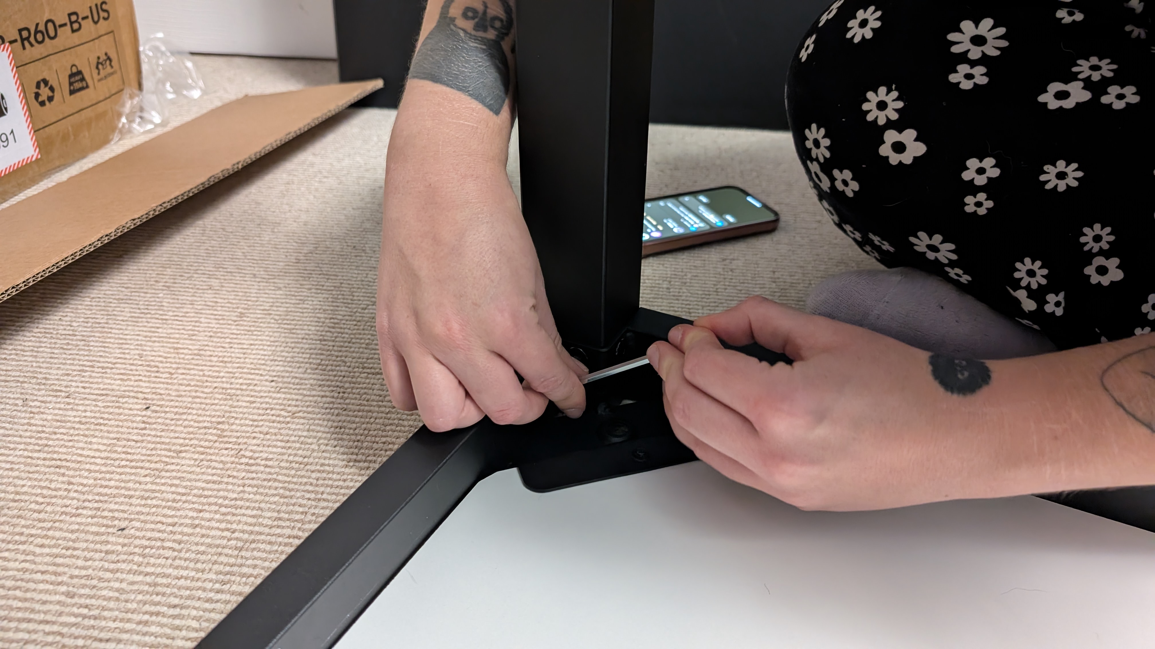 Closeup of a person's hands tightening a screw on a desk leg with a hex key while assembling the Eureka Ergonomic GTG Wave gaming desk.