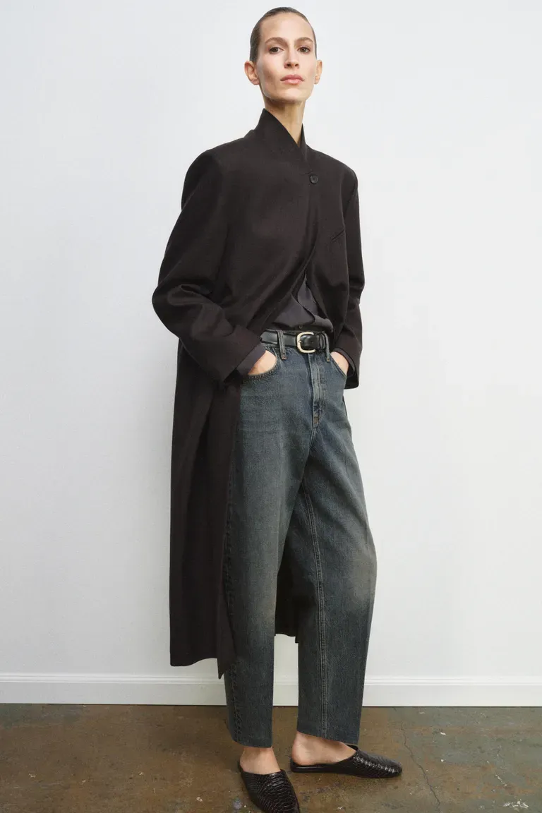 Model wears long wool coat, blue jeans and loafers