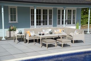 Large outdoor patio sectional sofa between a pale blue house and porch and a pool.