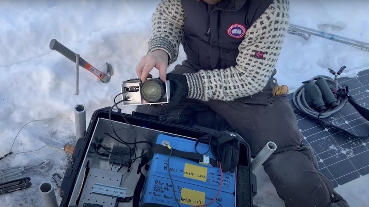 A researcher prepares a camera inside a rugged box with extra batteries in the snow