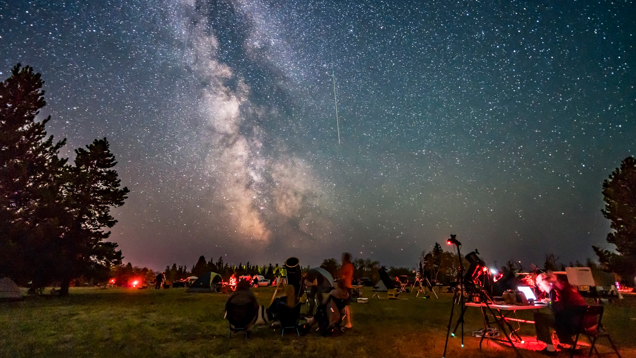 Several astronomers gathered in a field under the night sky with telescopes