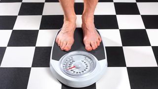 A shot of man's feet standing on bathroom scales on a black and white tiled floor