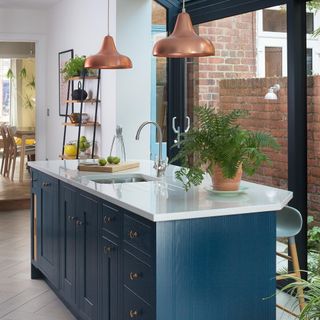 dark blue cabinet with drawers and white worktop, brass pendants