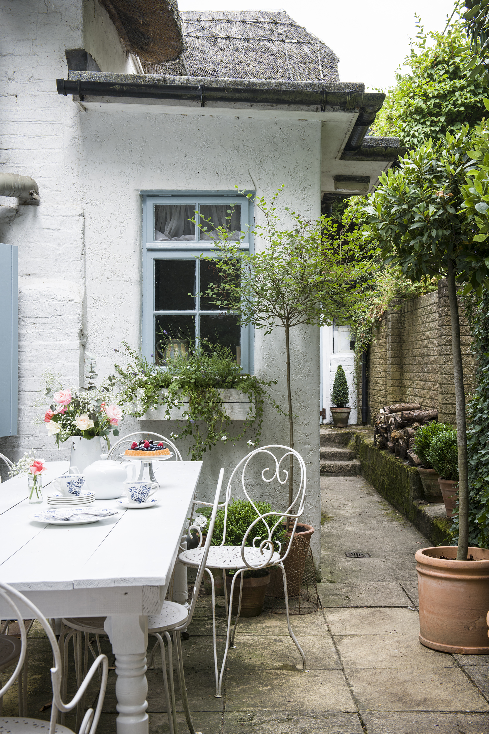 Cottage garden with wrought iron white painted dining chairs, patio floor and border planting