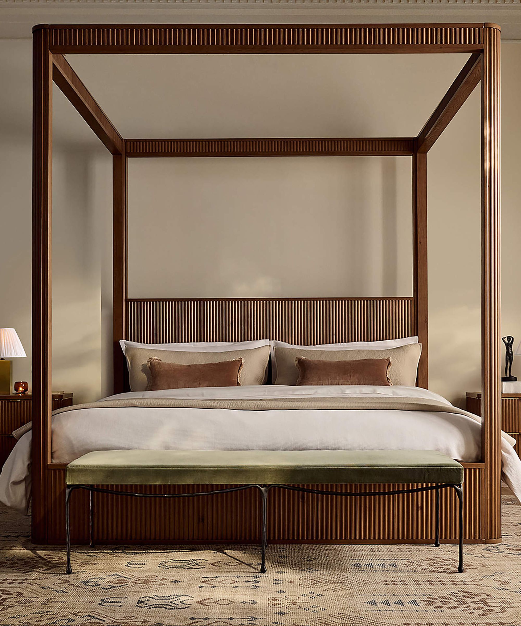 warm beige bedroom with a wooden fluted four posted bed and wrought iron foot of bed bench